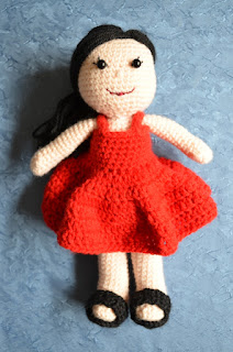 Kwokkie Doll is standing up, wearing a red sleeveless sundress and black sandals against a blue background.