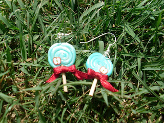 Boucles d'oreille en forme de sucettes bleu-vertes en pâte Fimo, ornées d'un ruban rouge et d'une petite tranche de pomme, déposées dans l'herbe