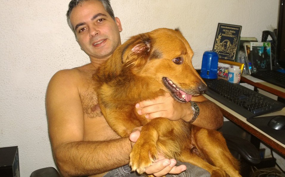 DEMÉTRIO EM SEU ESCRITÓRIO, COM SEU CACHORRO DE ESTIMAÇÃO, LENDO O LIVRO DO KUERINE.