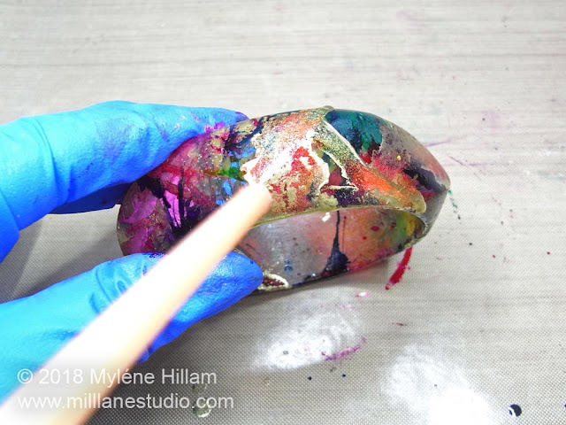 Blowing the gold alcohol ink around the bangle so that it mixes with the coloured alcohol inks and creates a marbled effect.