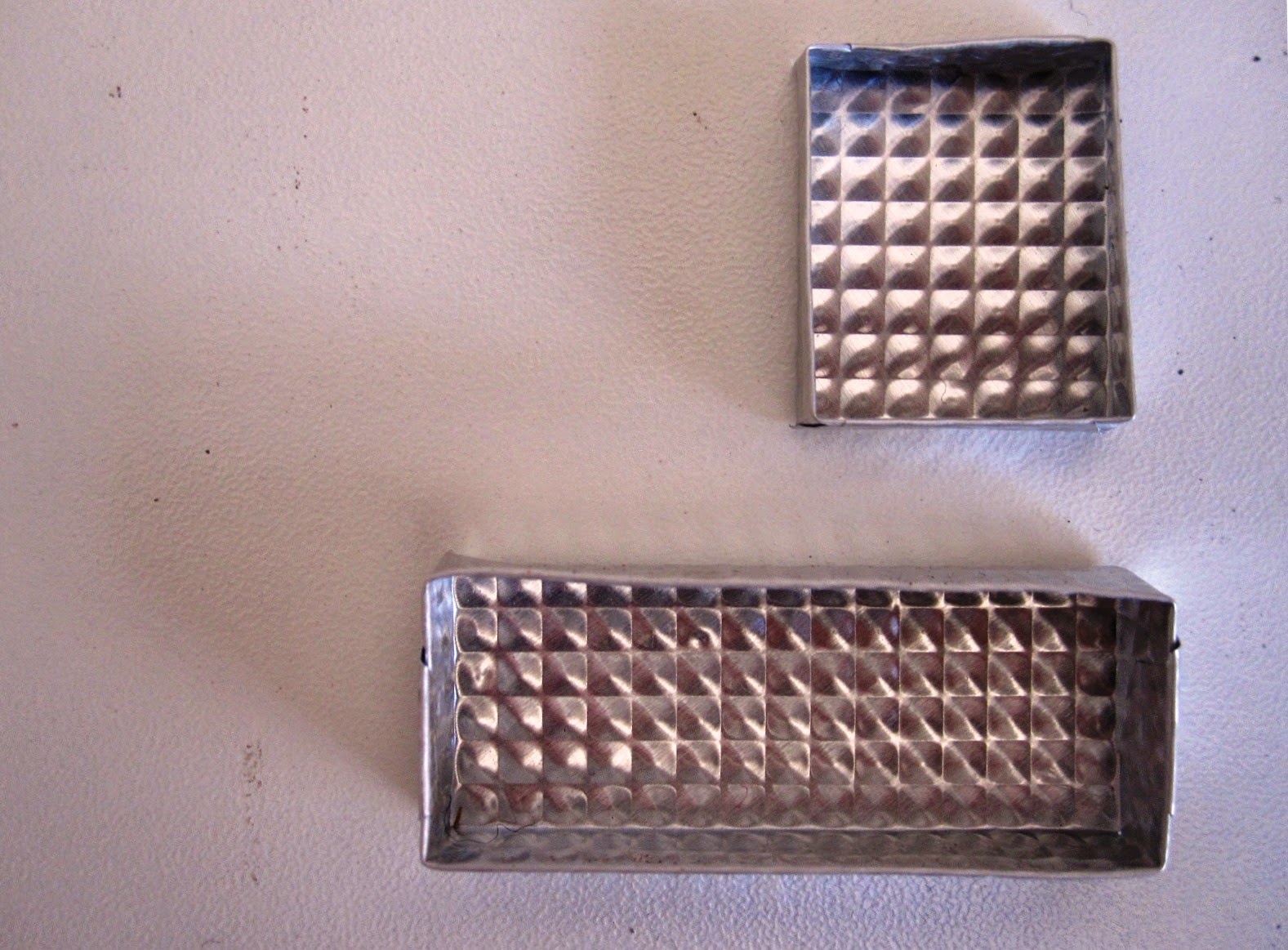 Two silver-coloured embossed metal dolls house miniature trays, one rectangular and one square.
