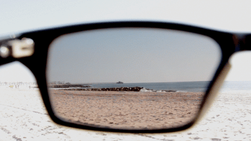 Bir güneş gözlüğü camından dalgaların kıyıya vuruşunu gösteren sinemagraf resim