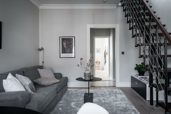 Salón decorado en tonos neutros con silla mariposa, escalera y suelo de madera natural