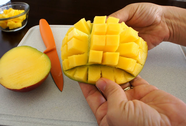 A A hand holding a slice of mango pushing the sliced cubes out away from the skin