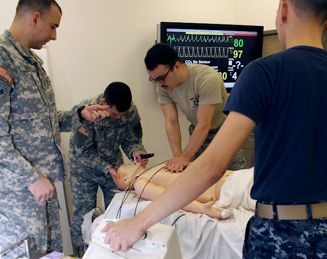 Four men in military uniform learn on a dummy in a hospital room. USU medical students are trained in basic life support, advanced cardiac life support, pediatric life support, and advanced trauma life support as part of their USU education.  (USU photo)