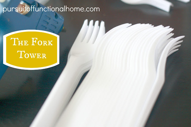 The Fork Tower Project. Blue Hot Glue Gun and white forks on top of the table. 