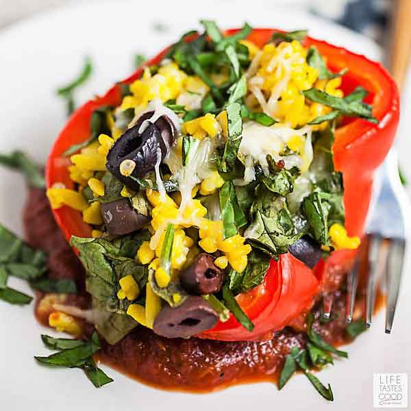 Vegetarian Stuffed Peppers with Orzo Pasta are full of Mediterranean flavors! These stuffed peppers are healthy, easy to make. and will kick your dinner rut to the curb! #LTGrecipes #stuffedpeppers #vegetarian #meatlessmonday #dinnerrecipe Red pepper stuffed with orzo pasta, spinach, & olives and topped with parmesan cheese on a white plate - Vegetable Stuffed Peppers with Orzo Pasta