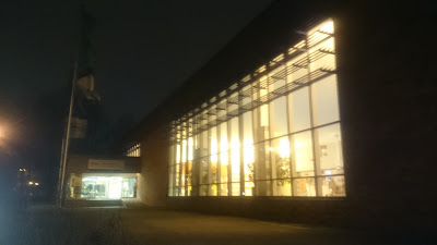 Die Ernst-Thälmann-Schwimmhalle am Abend. Draußen es bereits dunkel. Die Halle leuchtet einladend in einem warmen Farbton,