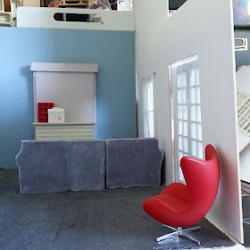One-twelfth scale modern miniature lounge in soft blue, grey and red with a sectional sofa, a fireplace and french doors.