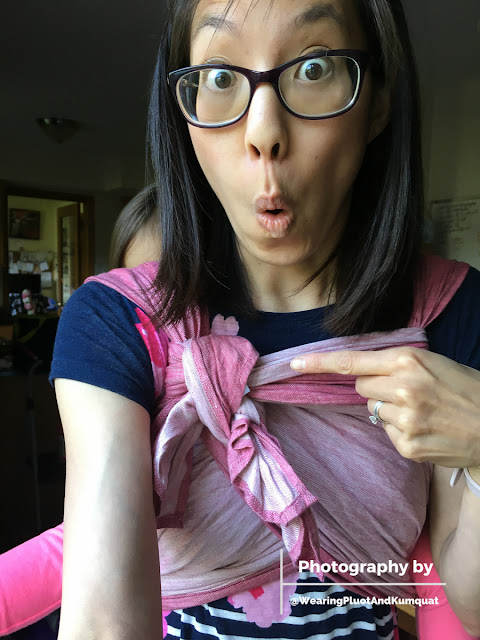 [Image of me, a light tan skin bespectacled Asian woman with dark brown hair, making a wide-eyed surprised face and pointing at the itty bitty double knot from a finished rucksack back carry tied Tibetan with a preschooler on my back.]