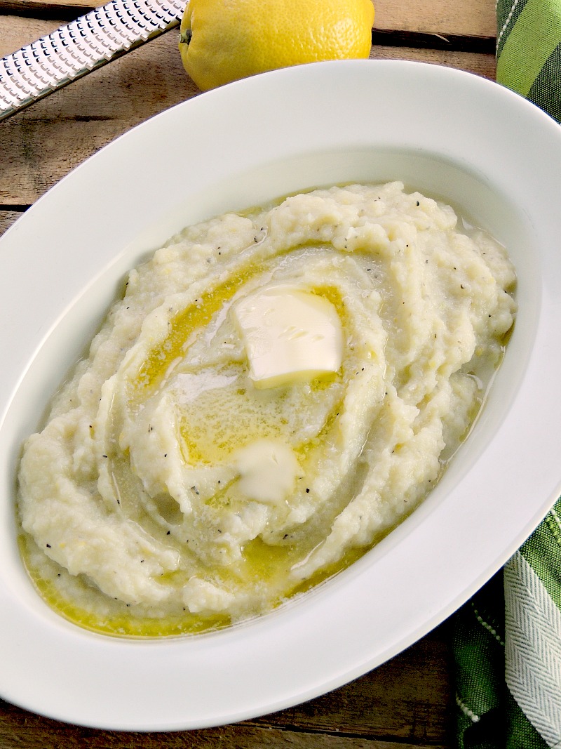 Lemon Garlic Mashed Cauliflower "Potatoes" topped with a pat of butter in a white bowl on a wooden background