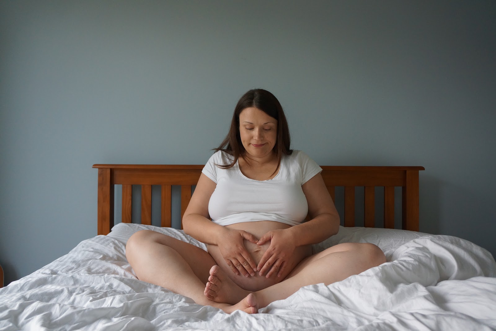 pregnant woman sitting on bed and cradling belly