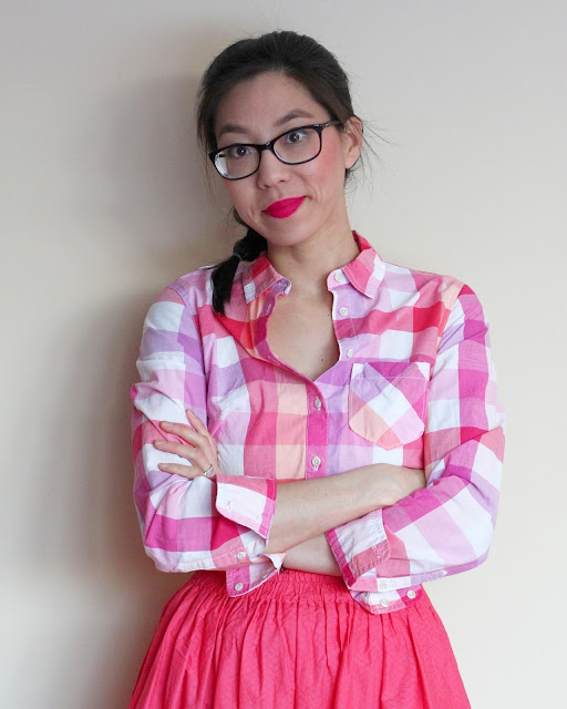 [Image of a tan skin bespectacled Asian woman wearing a plaid pink button down tucked into an elastic waist A-line coral skirt she made for herself years ago. Her arms are crossed. Her dark brown hair in a French braid. She’s got on her favorite hot pink lippie. With head slightly tilted to the side, she’s looking at you with a challenging smile and to be you because you are enough and you are worth it.]