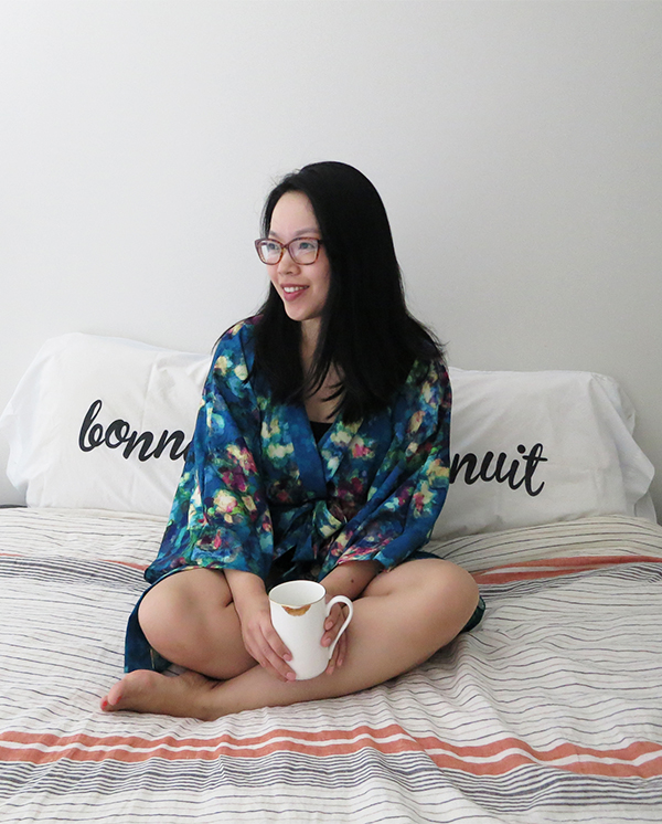 Vancouver blogger Solo Lisa wears a blue kimonette by Smash + Tess while sipping tea from a gold lipstick print mug in front of pillowcases that say 