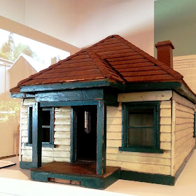 1930s vintage dolls' house bungalow on display in a museum gallery, showing the front and side.