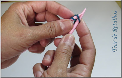 Foto mostrando o ponto formado na agulha direita sendo trazido para a agulha esquerda na montagem à francesa dos pontos da base do tricô
