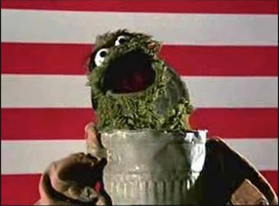 Oscar the grouch singing by his trash can with U.S. flag as backdrop.
