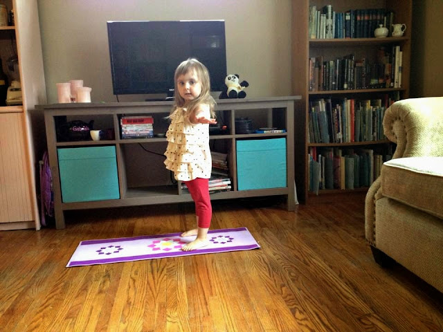 Photo of young girl standing on a yoga mat in the living room--with wooden floors