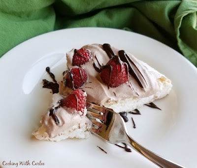 Turn a cloud into dessert. This dessert is both simple and amazing. A light and crisp meringue topped with cocoa whipped cream, fresh raspberries and a chocolate drizzle. Raspberry cocoa pavlova may be your new favorite dessert! fork taking the end off a slice of chocolate raspberry pavlova