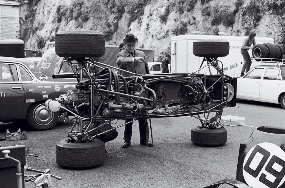 Un cotxe de F1 tombat de costat, sobre dues de les seves rodes, i així els mecànics poden treballar, la foto sembla dels 60.