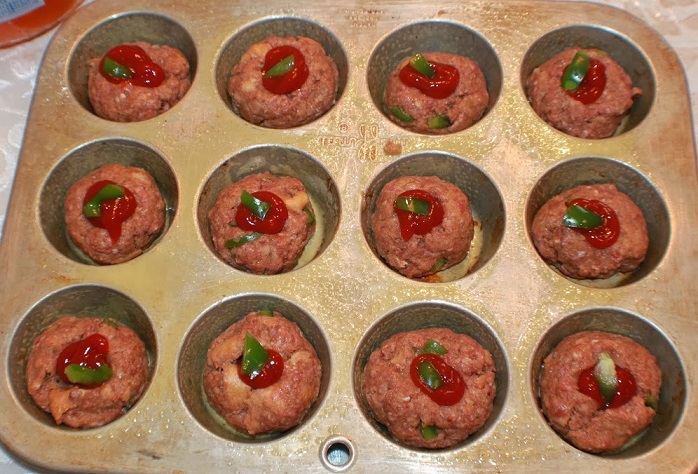 these cupcake tins are filled with how to make miniature raw meatloaves made in a cupcake tin for individual servings. These are on a white plate with ketchup and baked green peppers on top