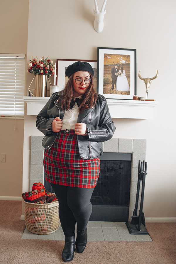 A plus size outfit consisting of a black beret, black faux leather moto jacket, white Peter Pan collar blouse, classic red tartan plaid mini skirt, black tight and black heeled chelsea boots