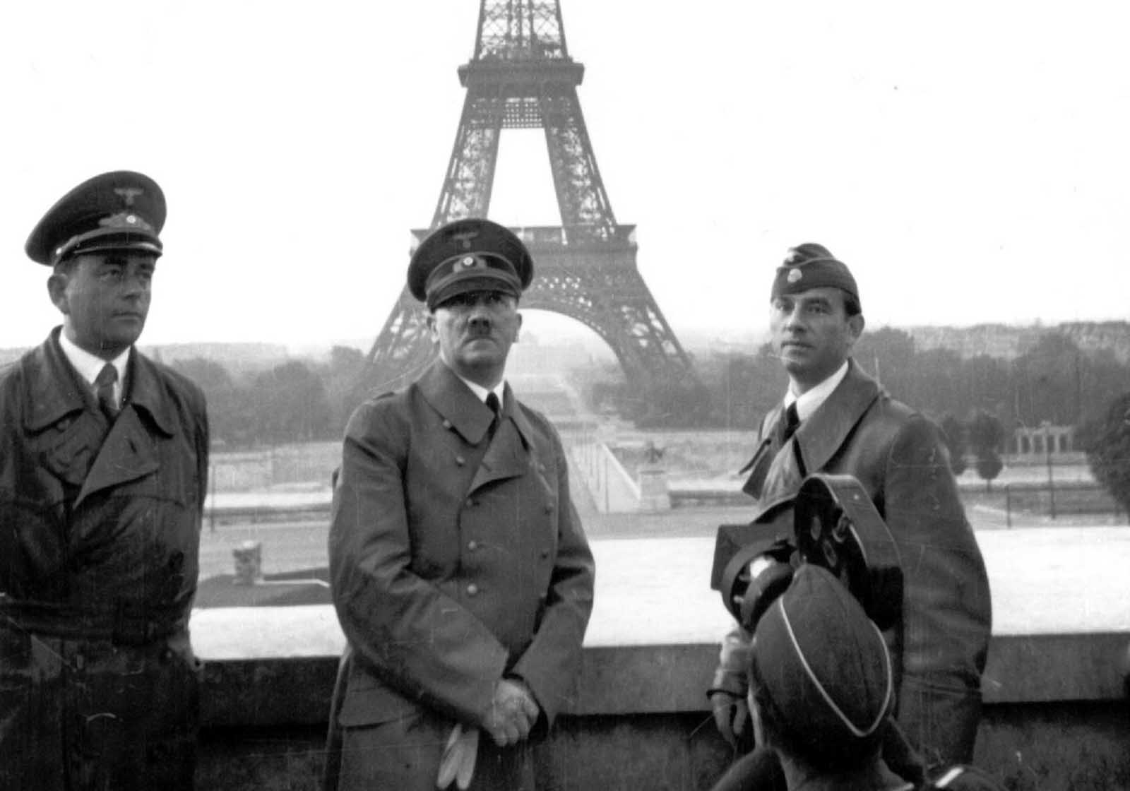 Adolf Hitler poses in Paris with the Eiffel Tower in the background, one day after the formal capitulation of France, on June 23, 1940. He is accompanied by Albert Speer, German Reichsminister of armaments and Hitler's chief architect, left, and Arno Breker, professor of visual arts in Berlin and Hitler's favorite sculptor, right. An unknown cameraman seen in the foreground is filming the event. Photo provided by the German War Department.