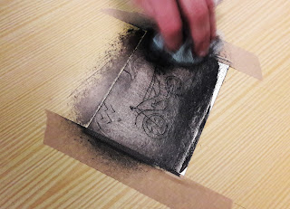 Um aluno movimenta de forma circular a tarlatana sobre a chapa da sua monotipia por forma a retirar o remanescente da tinta