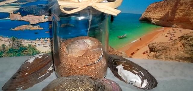 Glas mit Muscheln und Sand aus dem Urlaubsland dekoriert mit Urlaubskarten im Hintergrund DIY Deko mit Strandgut und Postkarten aus dem Urlaub
