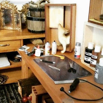 One-twelfth scale workbench top containing a cutting mat and various tools, including miniature tweezers, scissors and a dremmel.