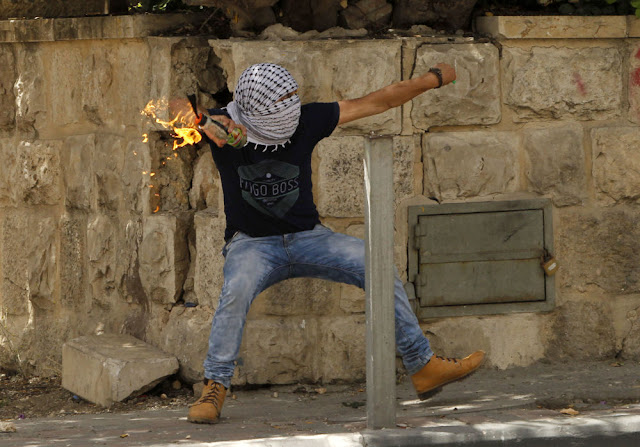 A Palestinian throws a petrol bomb towards Israeli security forces during 