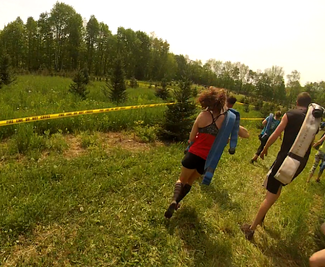 Athletes carry fire hoses over shoulders running through a field during the Hero Rush OCR