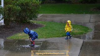 Boys splashing in puddles wearing rain coats and rain boots