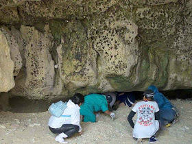 people crawling into a seaside cave