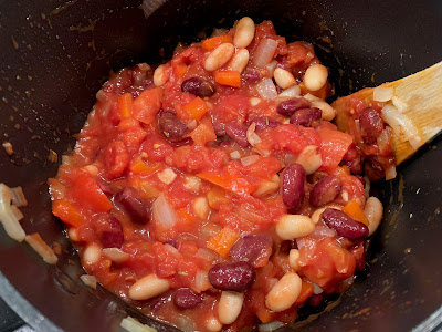 Tinned tomatoes added to beans, peppers and onion in a saucepan