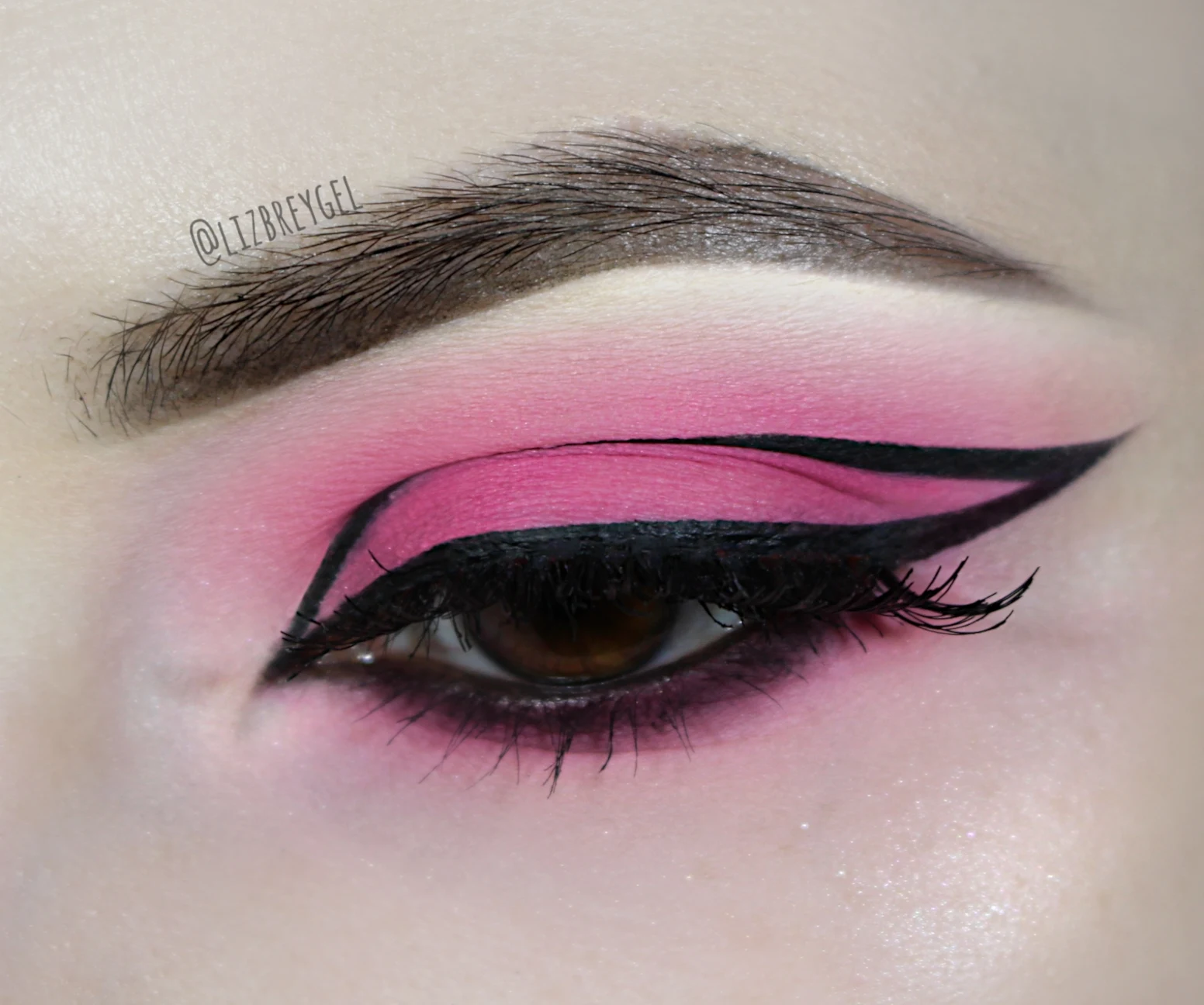 a close-up of a brown eye with a beautiful bubblegum pink eyeshadow and graphic eyeliner makeup look for Valentine's day