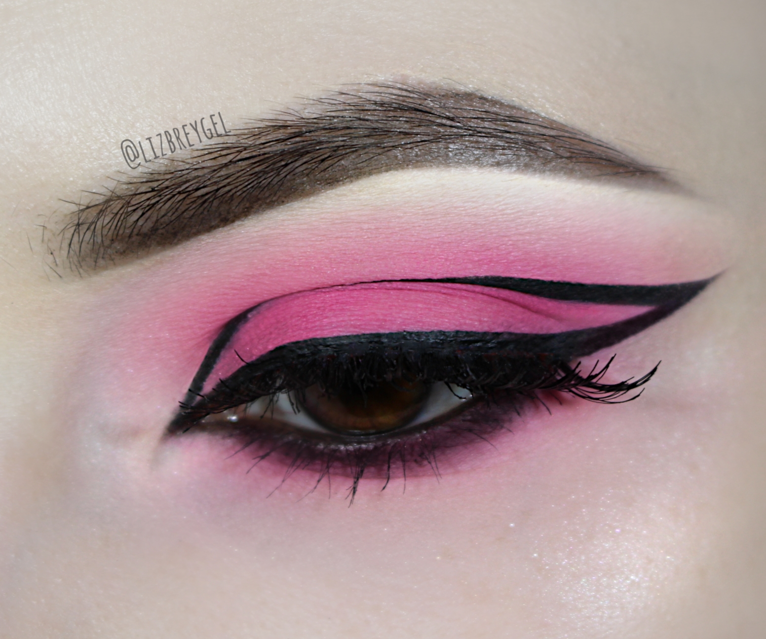 a close-up of a brown eye with a beautiful bubblegum pink eyeshadow and graphic eyeliner makeup look for Valentine's day