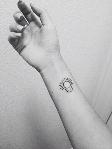 Uma versão simplificada de uma meia-lua e o sol são renderizados na portador de pulso, com tinta preta e em este de tatuagem.