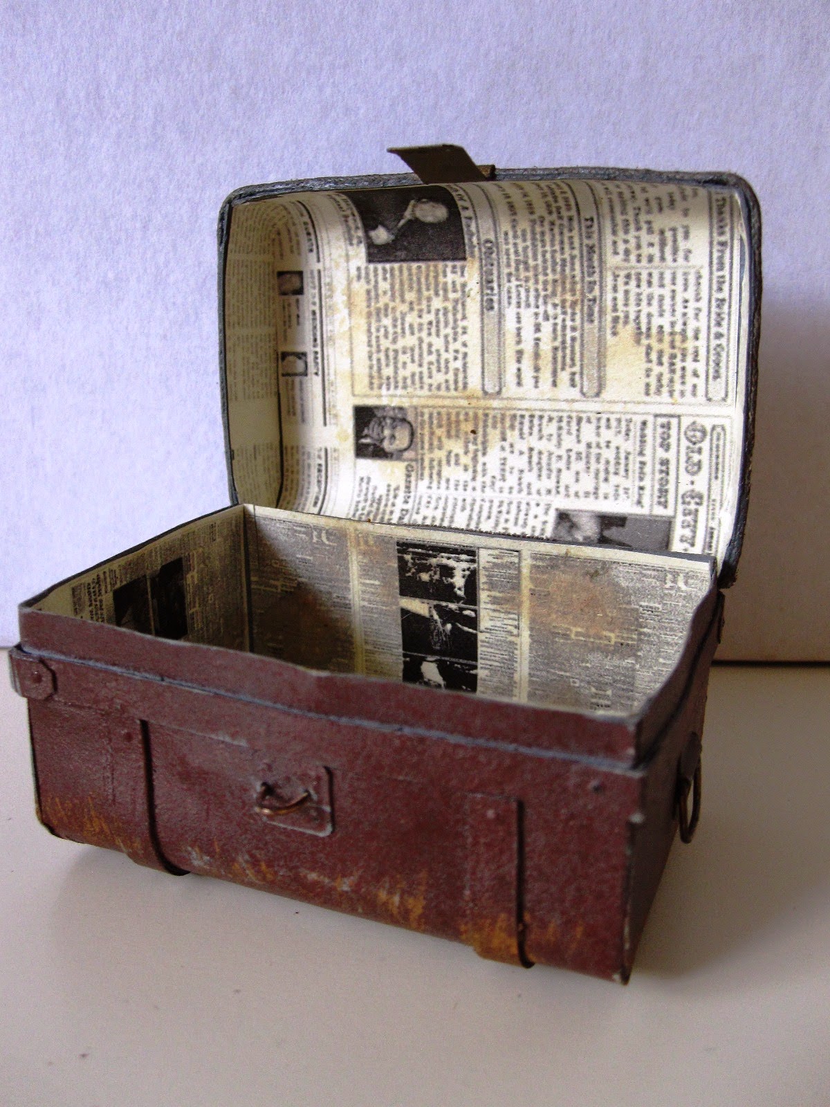 Open miniature vintage tin trunk, showing newspaper lining.