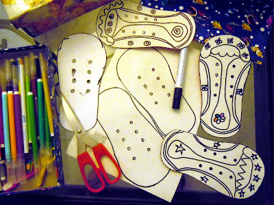 Inicio del proceso de creación de zapatos de cartón: siluetas blancas pintadas con rotulador negro, junto a tijeras y rotuladores de colores. Fotografía ©Selene Garrido Guil