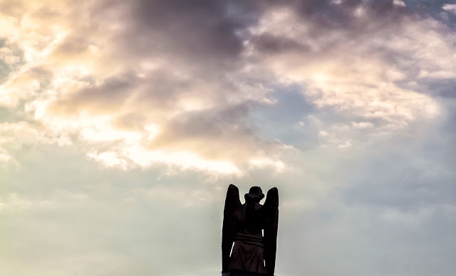 Allá en el cielo Un angel de cemente emergiendo hacia un cielo con nubes
