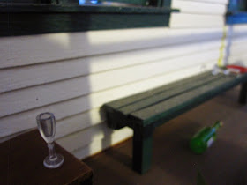 Modern dolls' house miniature verandah with a wine bottle, plate and wine glasses strewn around.