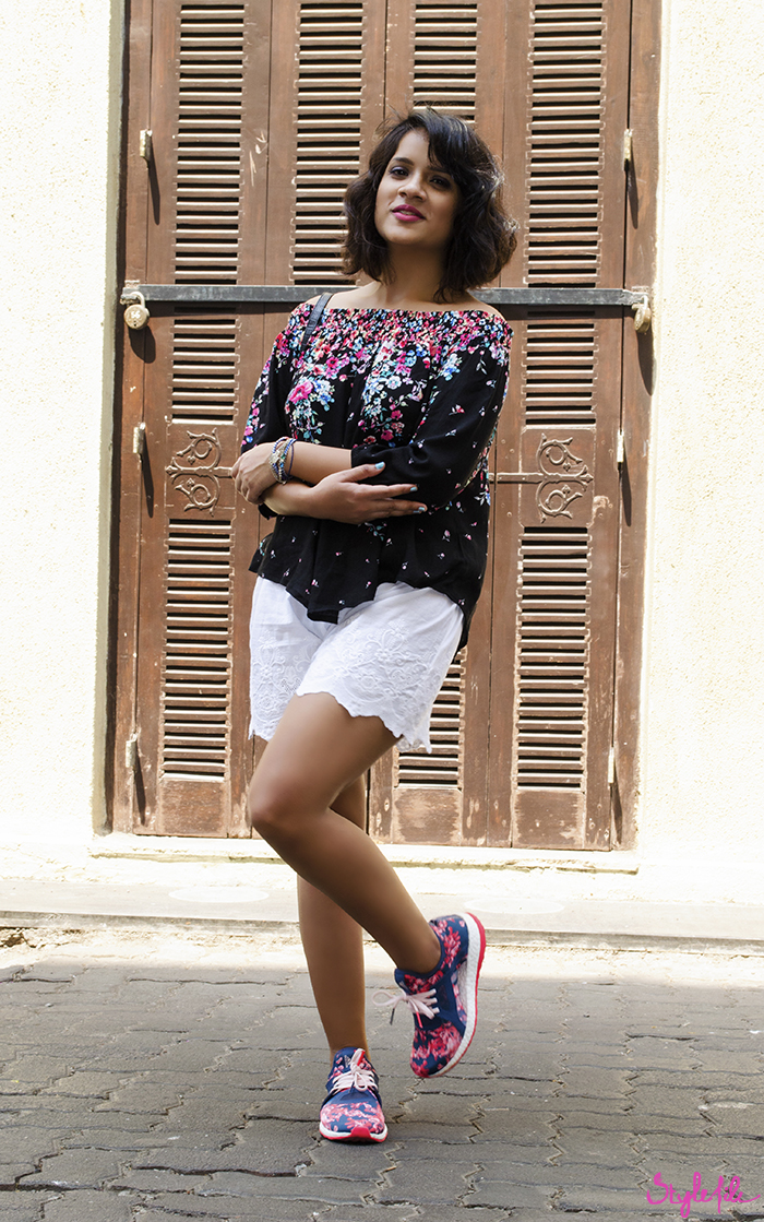 Style File blogger Dayle Pereira showcases her womens fashion outfit with a cold shoulders floral blouse, cutwork shorts, printed sneakers, mini bag and a wavy long bob with coral lips and blue nails
