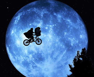 Imagen con Elliot transportando a ET en su bicicleta en sombras. Al fondo una gran luna llena