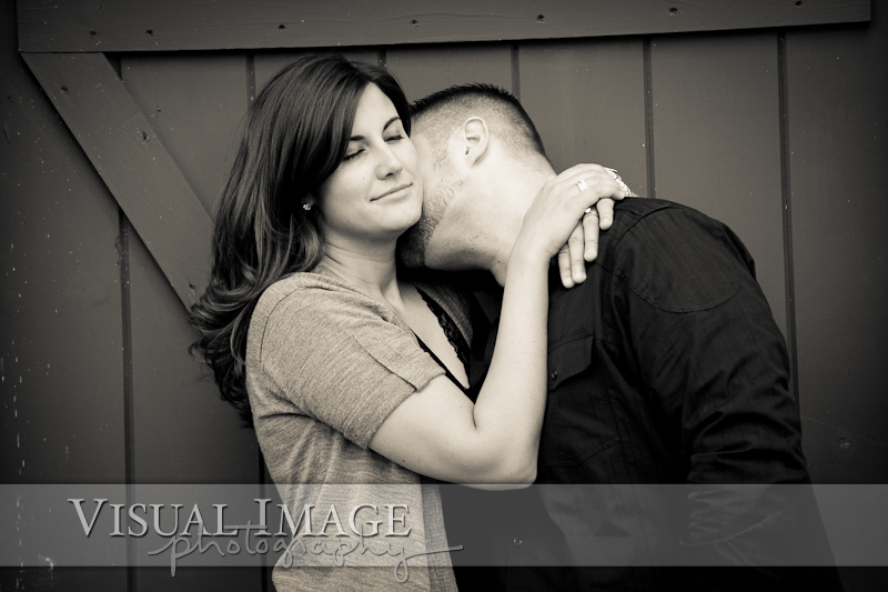 black and white photo of woman with eyes closed while fiance kisses her neck