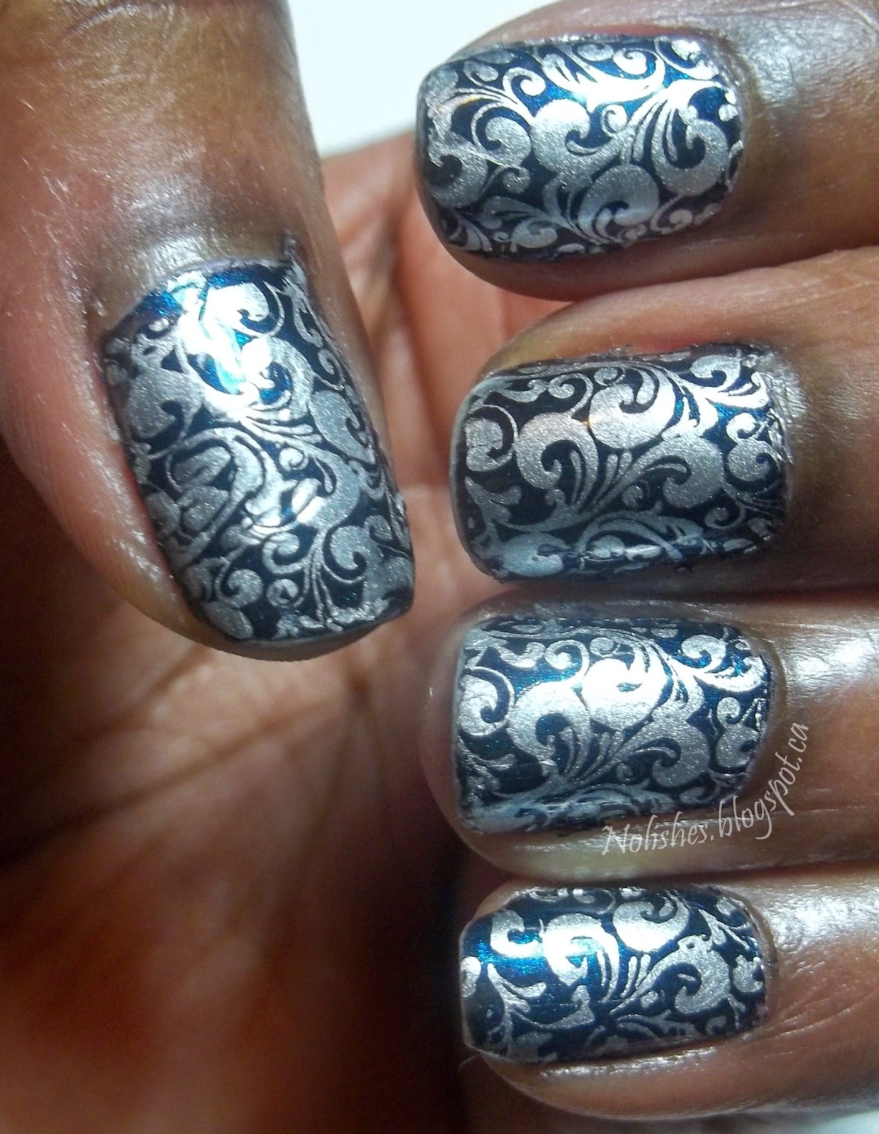 A basic nail stamping manicure created with a dark teal base polish stamped with a dense filigree pattern in silver.