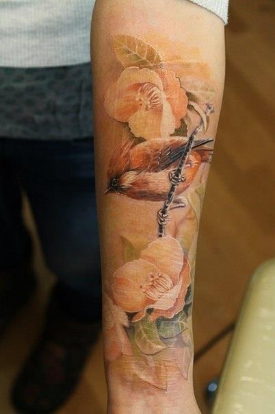 Kolorowy tatuaż ptaka i kwiatów na przedramieniu