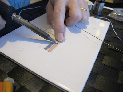 Woman placing the tip of a soldering iron onto a length of wire on a run of copper tape.