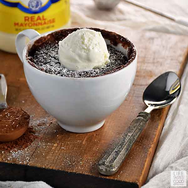 A Gooey Chocolate Mug Cake satisfies your chocolate cravings quicker than a hot knife through butter! Warm, chocolaty deliciousness made all in one mug in about a minute. What are you waiting for? You need chocolate and this microwave mug cake is the answer! #mugcake #chocolate #dessertrecipe #easyrecipe White mug with gooey chocolate mug cake topped with a scoop of vanilla bean ice cream on a rustic wood board