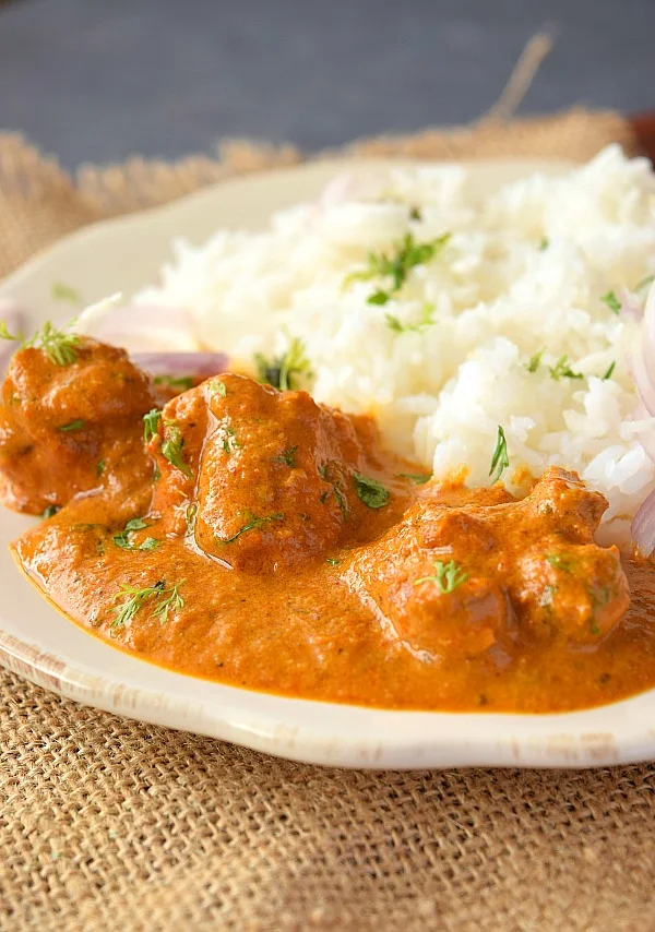 A white plate serving creamy delicious Chicken Tikka Masala with steamed rice